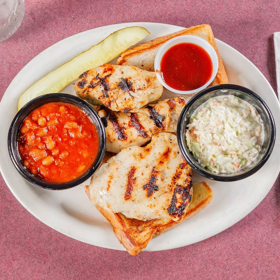 Grilled chicken tenders on toast with baked beans, coleslaw, a pickle spear, and BBQ sauce.
