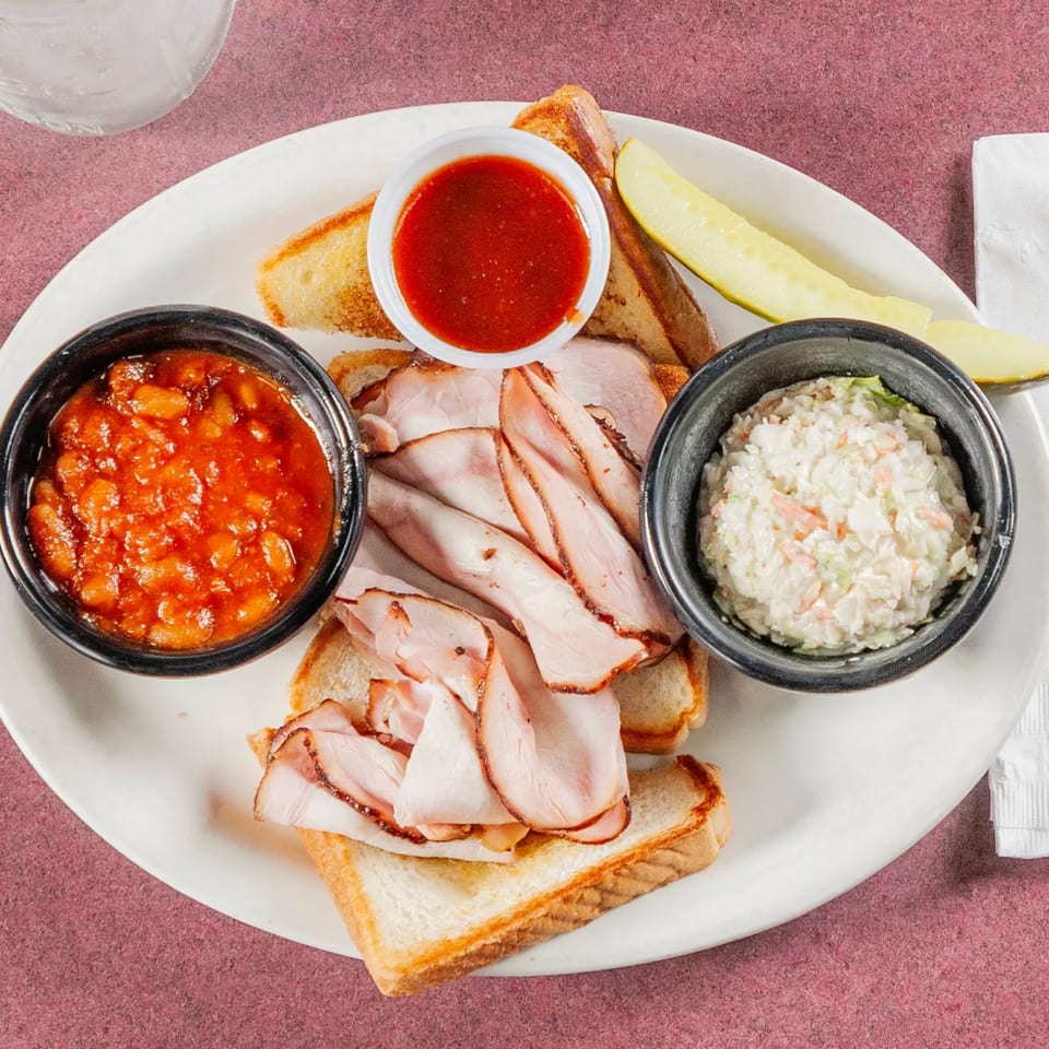 Jerry Neel's Bar-B-Q turkey plate with baked beans, coleslaw, toast, BBQ sauce, and a pickle.
