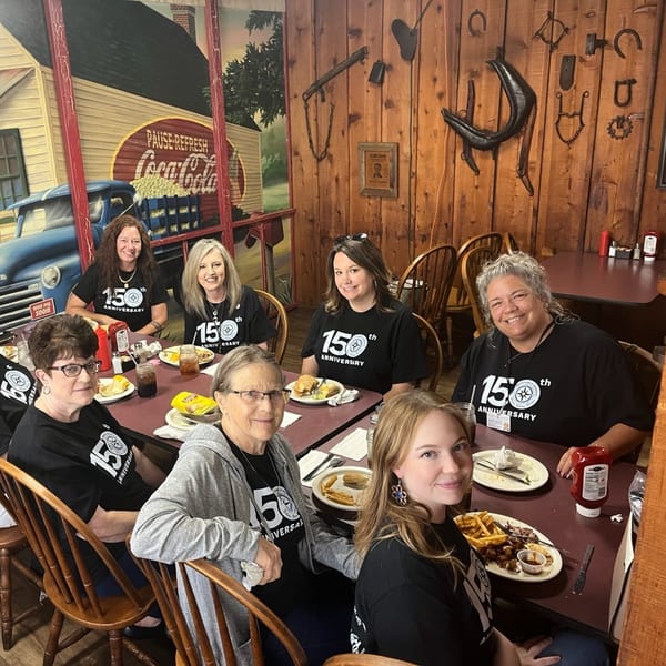 Seven women in black 150th Anniversary shirts dining at Jerry Neel's Bar-B-Q, Catfish, & Catering.