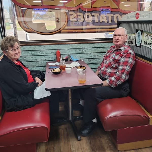 Two elderly customers seated in red booths at Jerry Neel's Bar-B-Q, with food and drinks on the table.