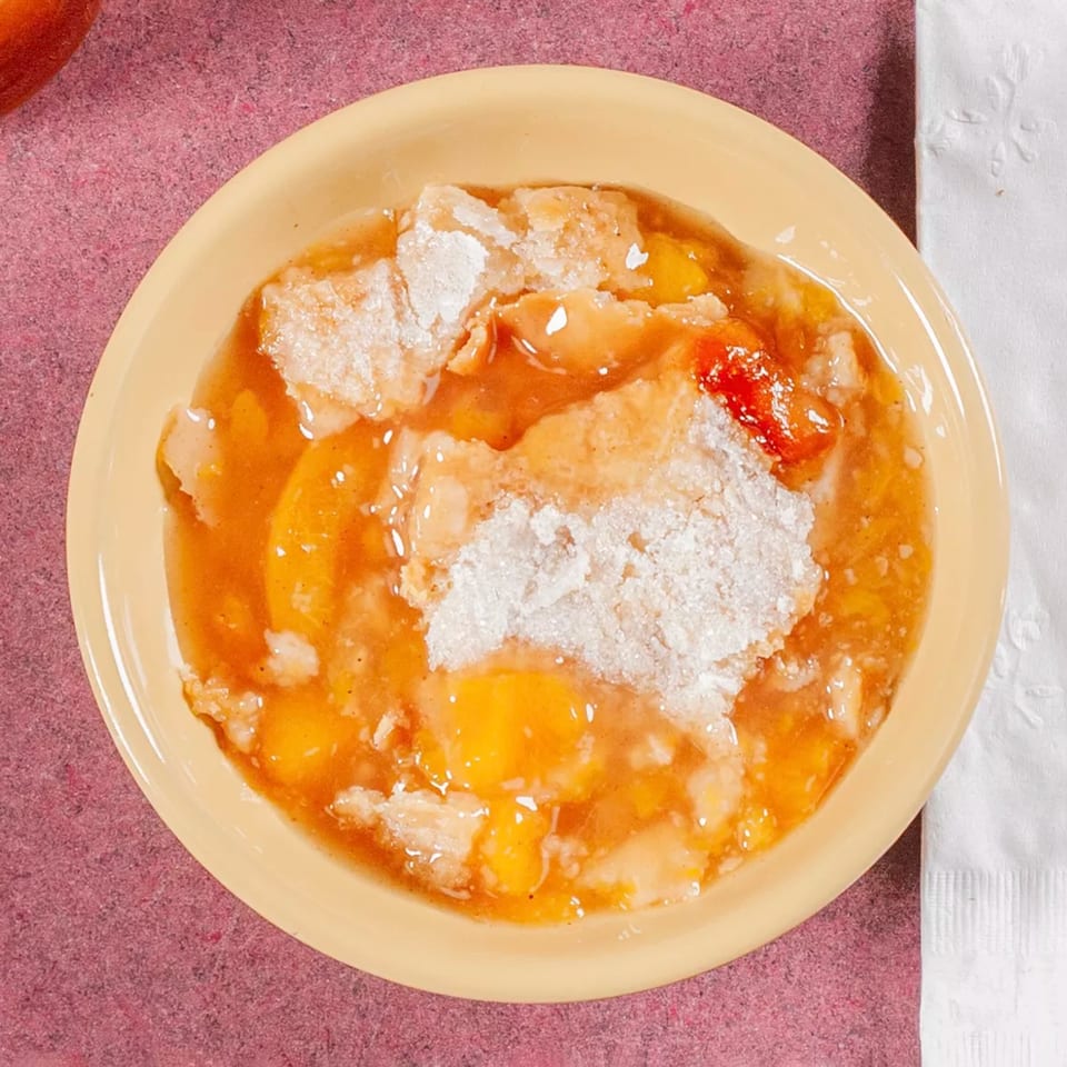 A yellow bowl of peach cobbler with a sugary crust, from Jerry Neel's Bar-B-Q.