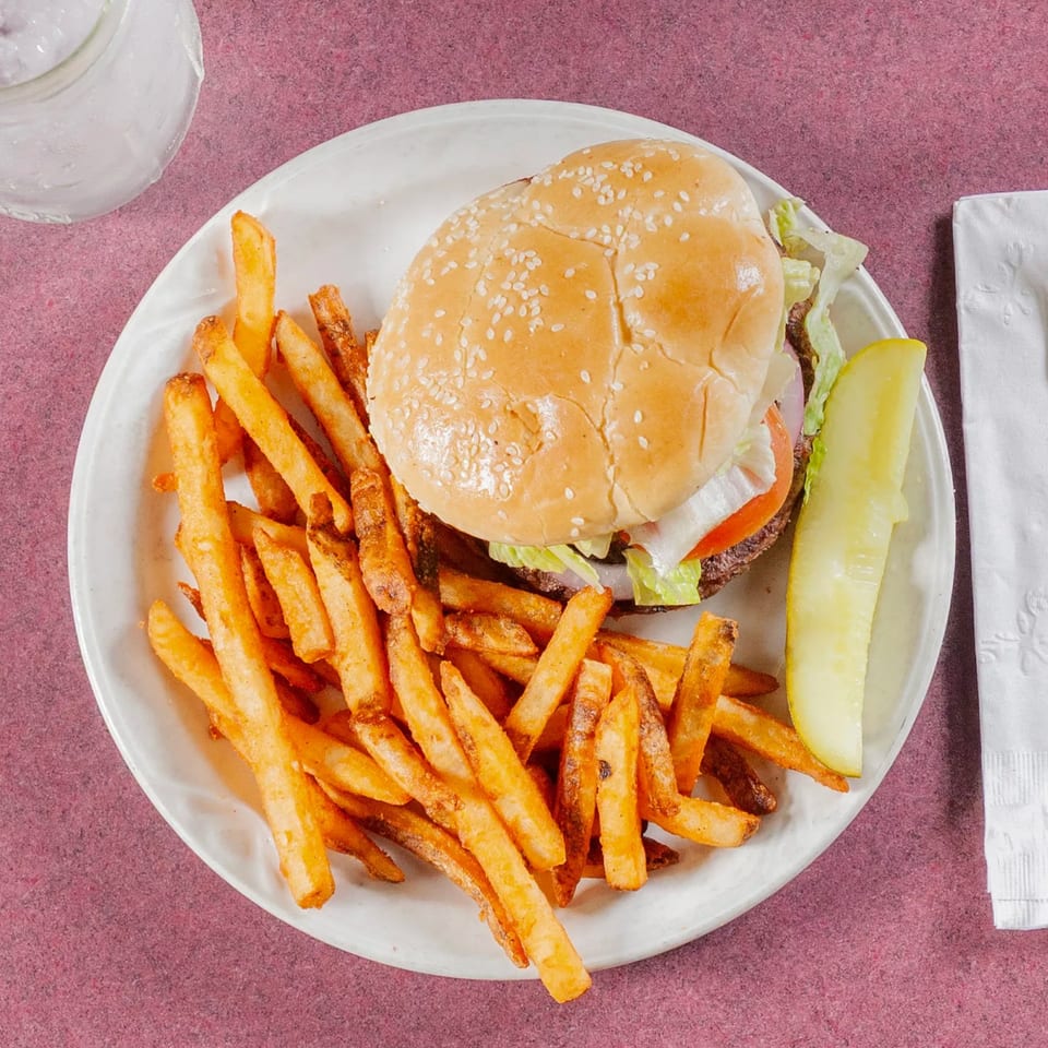 A hamburger with lettuce, tomato, and onion, served with fries and a pickle spear.