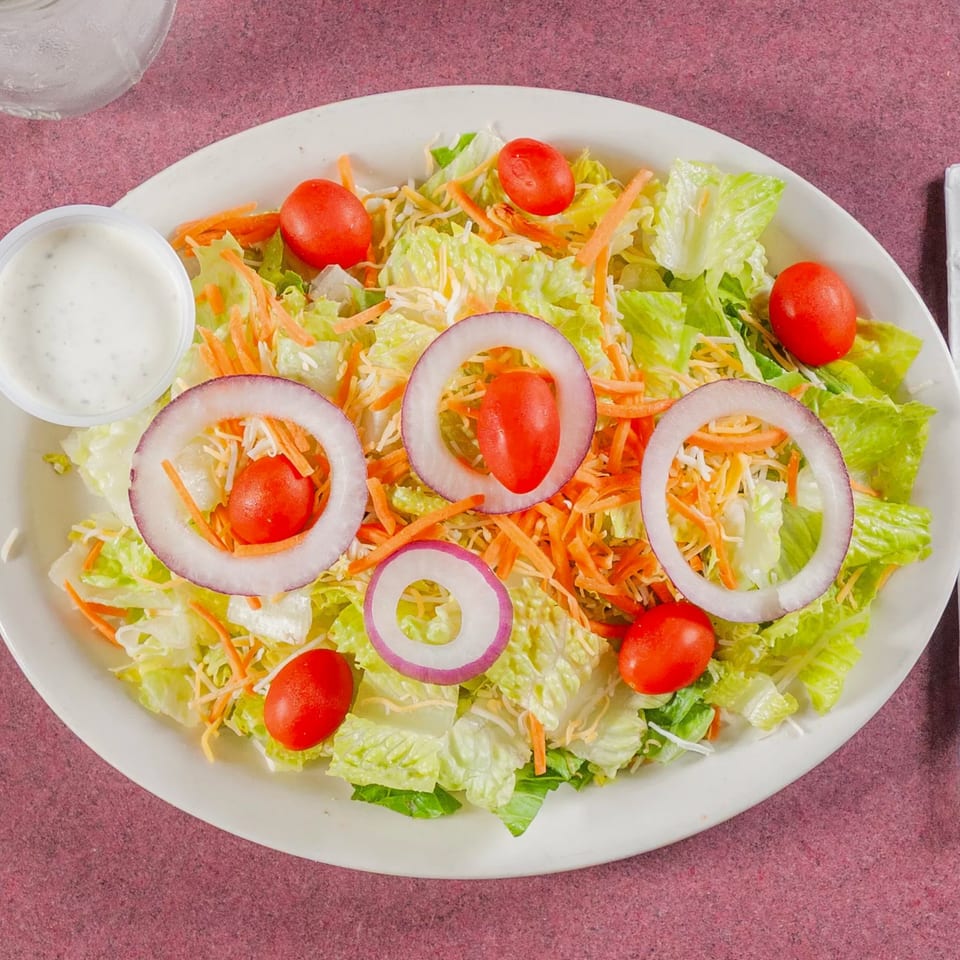 Fresh garden salad with lettuce, shredded carrots, cherry tomatoes, red onion rings, and ranch dressing.