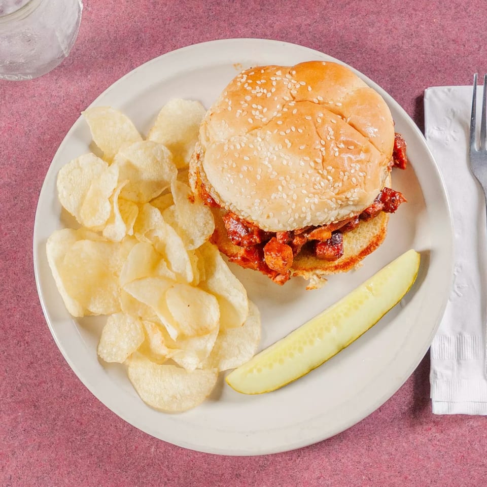 Jerry Neel's Bar-B-Q sandwich with potato chips and a pickle spear on a white plate.